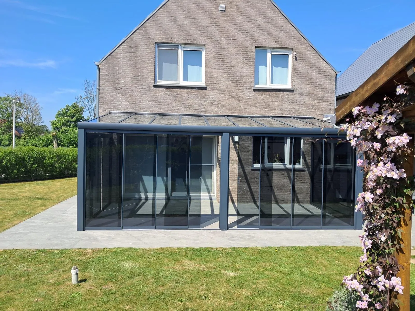 Aanbouwveranda met getinte beglazing en glazen dak aan een bakstenen woning